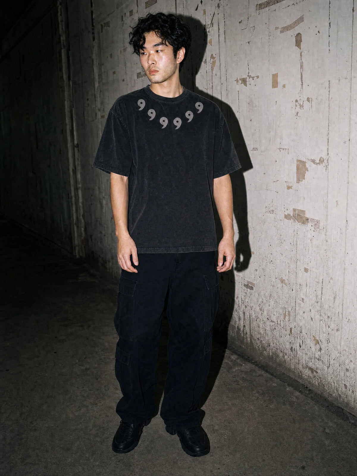 Model in a washed black Torazen tee printed with the six Rinnegan tomoe around the collar, against a concrete wall
