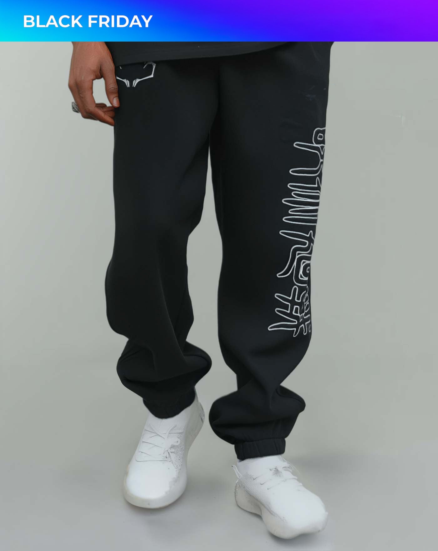Close-up of black anime-inspired streetwear sweatpants with white graphic side print, styled with white sneakers, showcasing relaxed street fit from Torazen’s latest drop.