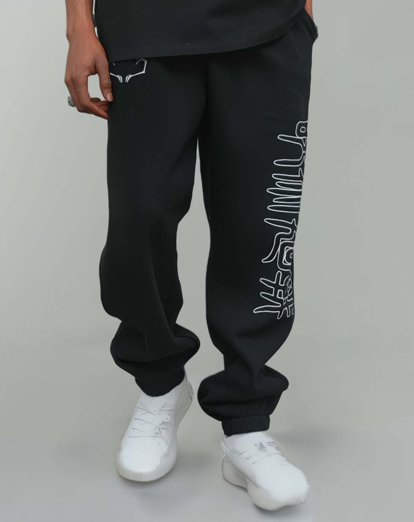 Close-up of black anime-inspired streetwear sweatpants with white graphic side print, styled with white sneakers, showcasing relaxed street fit from Torazen’s latest drop.